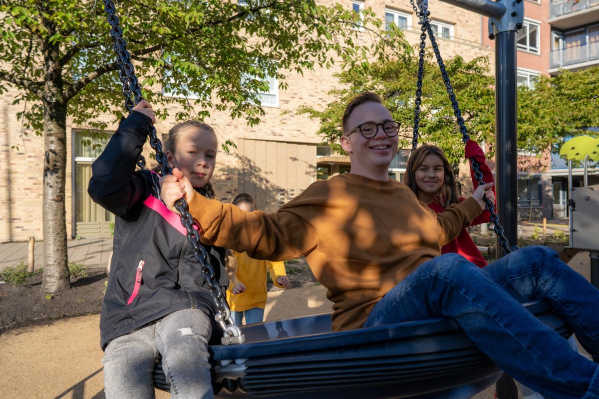Drie kinderen op een nestschommel in een inclusieve speeltuin
