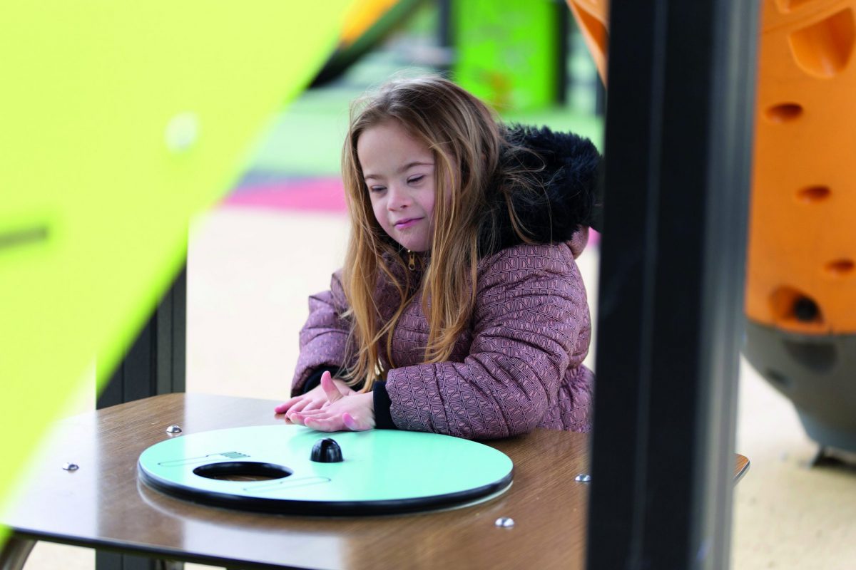 Meisje met beperking speelt aan interactief tafeltje in toegankelijke speeltuin