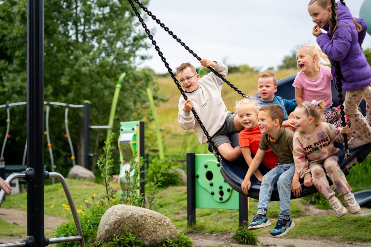 Groep kinderen samen op een nestschommel in groene speeltuin