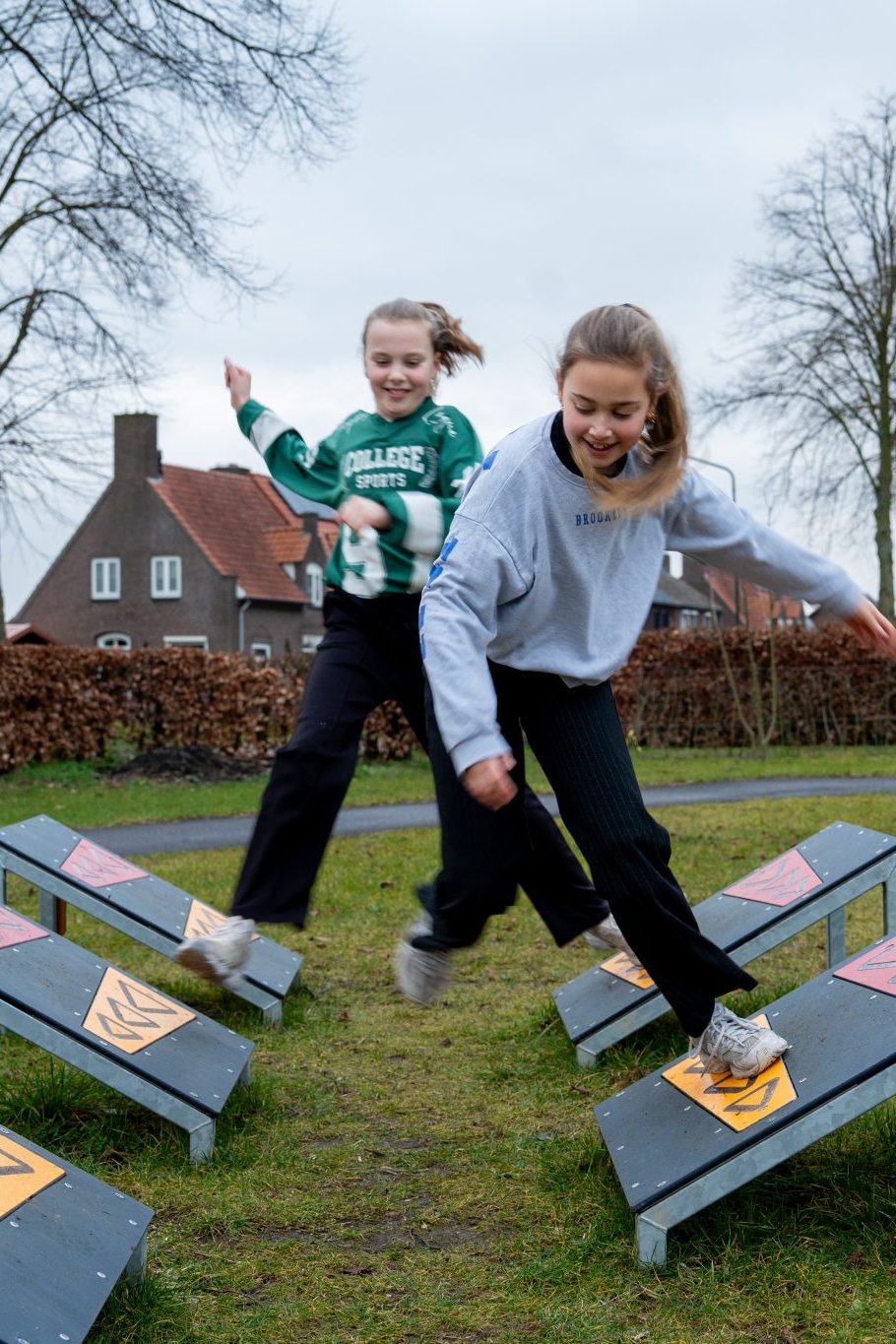 Twee meisjes bewegen over een parcours met schuine evenwichtselementen op een grasveld.